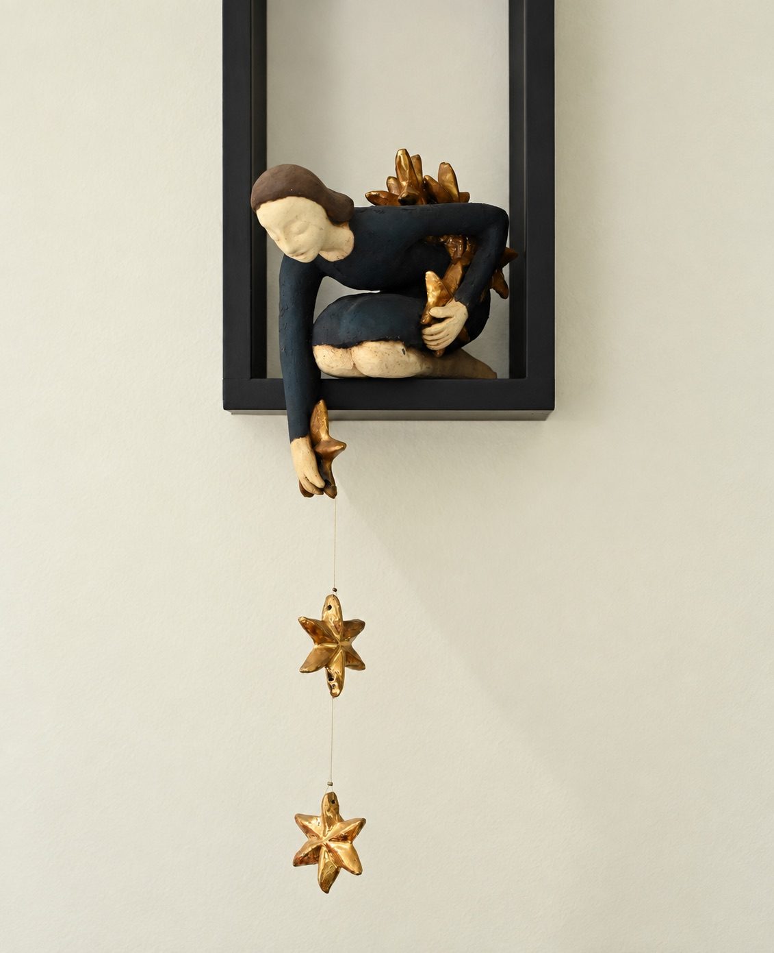 A small seated figure reaching down toward a hanging star, against a dark frame.